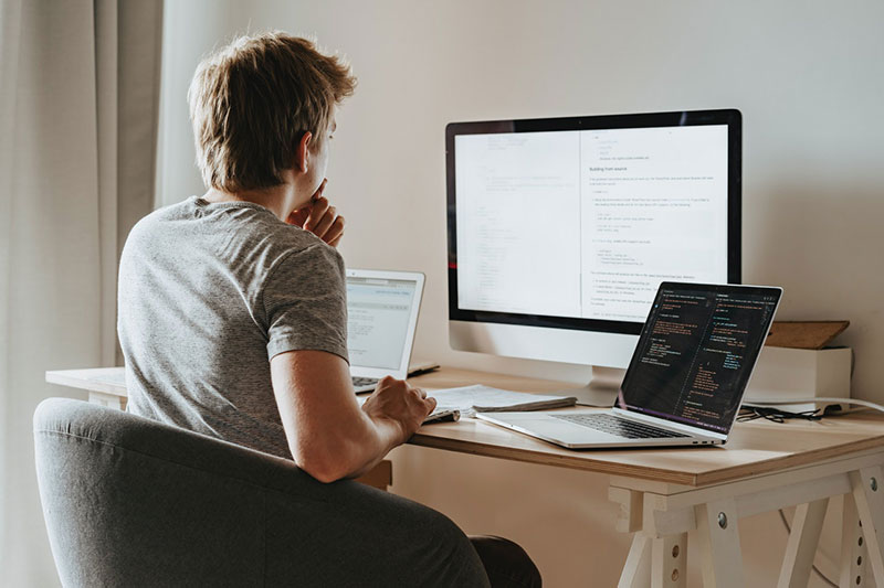 Person sitting at a desk with two laptops and a monitor