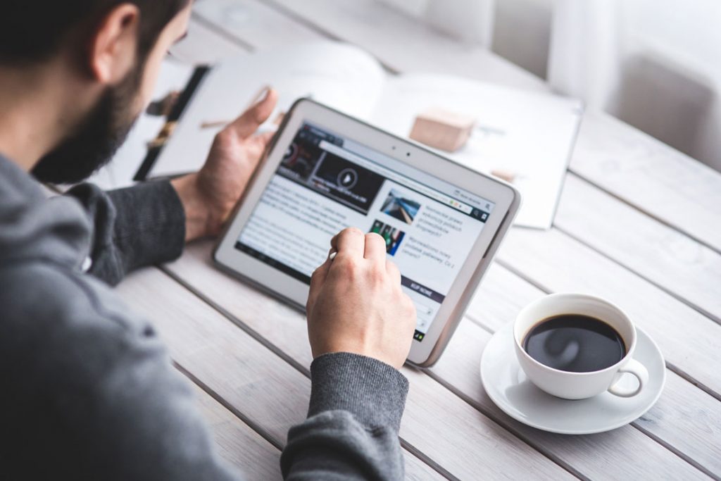 Person sitting at a table with a tablet in their hand and a cup of coffee to the side